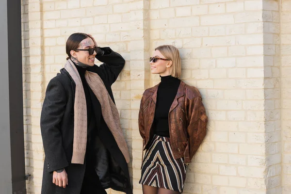 stock image happy tattooed man flirting with happy woman in trendy sunglasses near brick wall  