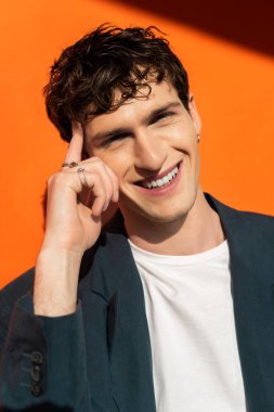 Portrait of smiling young man in jacket looking at camera on orange background with sunlight 