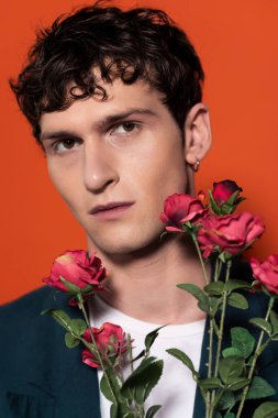romantical young man posing near roses isolated on red 