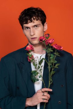 Fashionable model in blazer holding roses isolated on red 