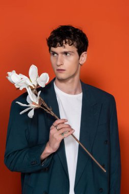 Man in blue jacket holding magnolia branch on red background