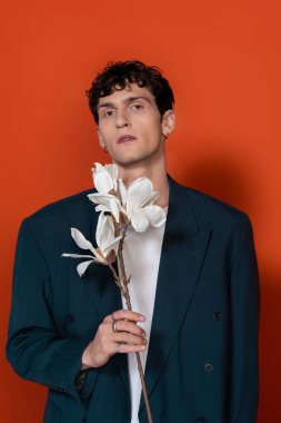 Stylish man in blue jacket holding magnolia branch on red background