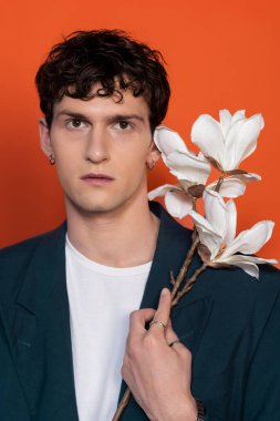 Portrait of stylish curly man holding magnolia branch isolated on orange