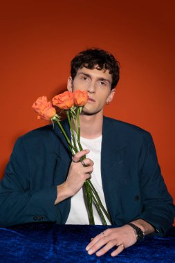 Trendy ma in blazer holding orange roses on red background