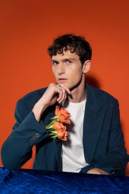 Stylish young man with flowers in sleeve of jacket looking at camera on red background