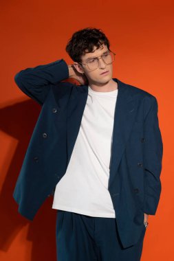 Stylish model in eyeglasses and blue suit posing on red background