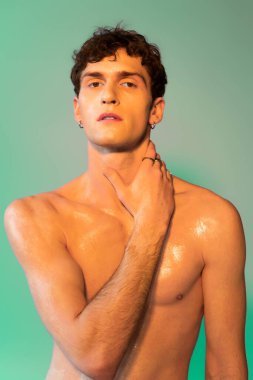 Portrait of stylish brunette man with oil on skin touching neck on green background