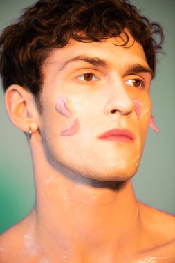 Portrait of young man with petals on face looking away on colorful background 