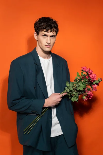 Brunette man in stylish outfit holding roses on orange background