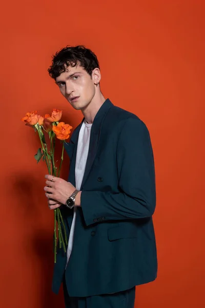 Trendy curly model holding orange roses for 8 march on red background