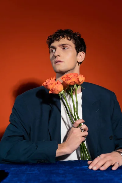 stock image Curly man in blazer and t-shirt holding orange flowers on red background