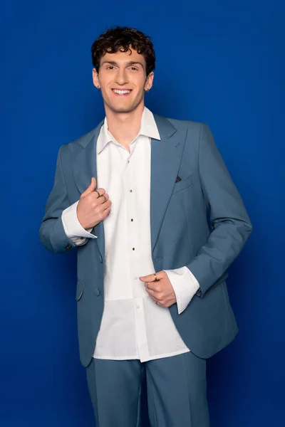 stock image Curly man in stylish suit smiling at camera on blue background 