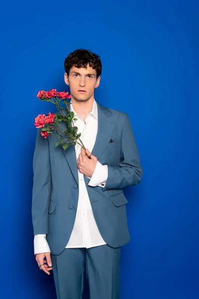 stock image Curly man in suit holding red flowers on blue background 