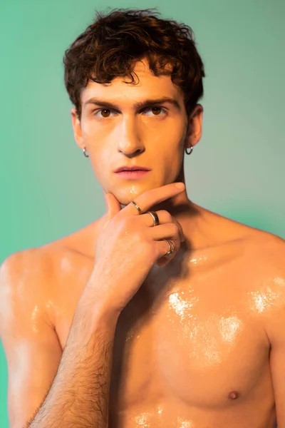 Portrait of shirtless man with oil on skin looking at camera on green background
