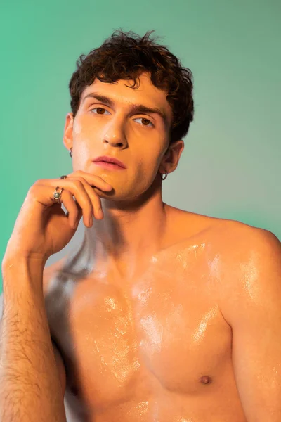 Portrait of young shirtless man with oil on skin looking at camera on green background