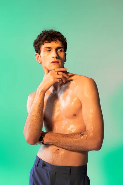 Shirtless man with oil on body posing and looking away on green background
