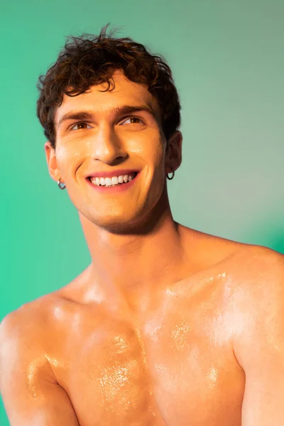 Portrait of smiling shirtless man with oil on skin on green background
