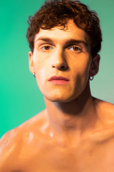 Portrait of shirtless brunette man with oil on skin looking at camera on green background