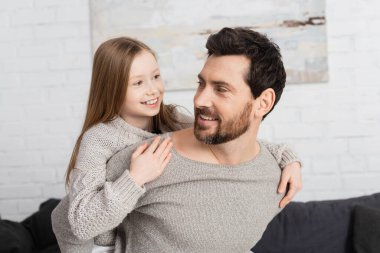 cheerful girl embracing bearded father and smiling at home