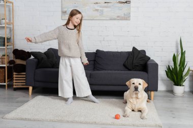 full length of joyful child playing with labrador dog on carpet in living room 