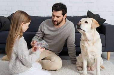Kız, babamla labrador köpeğinin yanında oturma odasındaki halıda oynarken göz farı ile palet tutuyor.