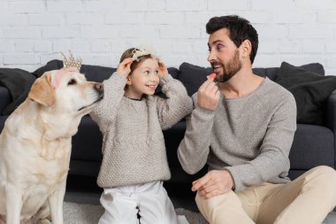 Labrador 'un yanında oturmuş babama dudak parlatıcısı sürerken mutlu bir kız. 