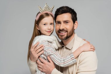 portrait of happy father and daughter in crown smiling while looking at camera isolated on grey 