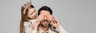 cheerful kid in crown covering eyes of bearded father isolated on grey, banner 