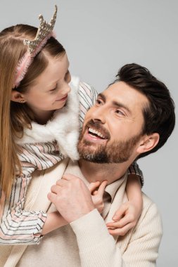 happy kid in crown hugging positive father with beard isolated on grey  clipart