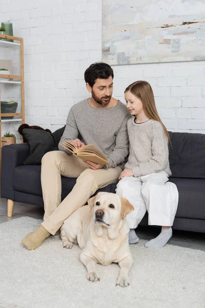 Bearded Man Showing Book Smiling Daughter While Sitting Couch Labrador —  Fotos de Stock