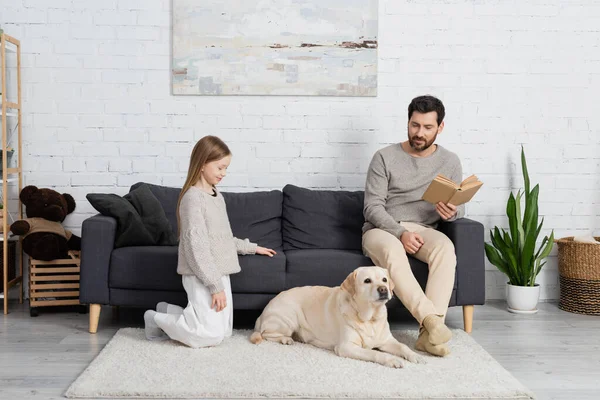 Bearded Man Book Sitting Couch Happy Daughter Labrador Dog Lying —  Fotos de Stock