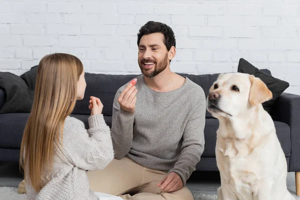 Smiling Bearded Man Holding Lip Gloss While Playing Daughter Labrador — Stock fotografie