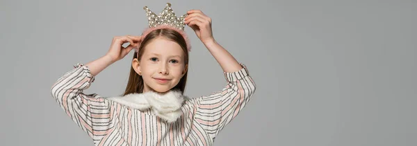 stock image happy girl adjusting crown on head and smiling isolated on grey, banner 