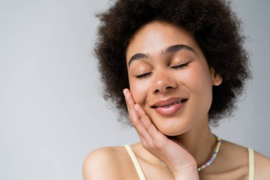 Yüzüne dokunan gülümseyen Afrikalı Amerikalı kadının portresi gri renkte izole edilmiş. 