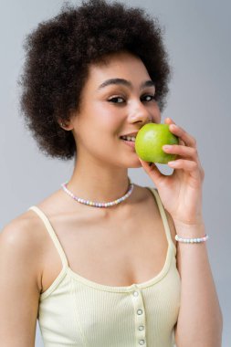 Gri üzerinde yeşil elma tutan gülümseyen Afrikalı Amerikalı kadının portresi. 
