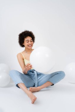 Çıplak ayaklı Afrikalı Amerikalı kadın gri arka planda balon tutuyor. 