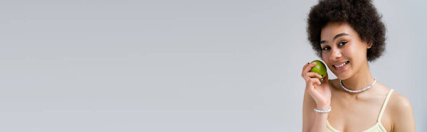 Африканская американка держит спелое зеленое яблоко, изолированное на сером, баннер 