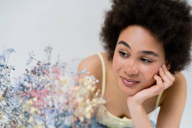 Güzel Afrikalı Amerikalı kadın gri renkte izole edilmiş bebek nefesli çiçeklere bakıyor. 