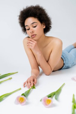Üstsüz Afro-Amerikan modeli gri arka plandaki bulanık lalelere bakıyor 