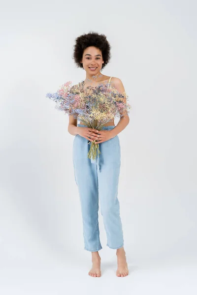 stock image Full length of barefoot african american woman holding baby breath flowers on grey background 