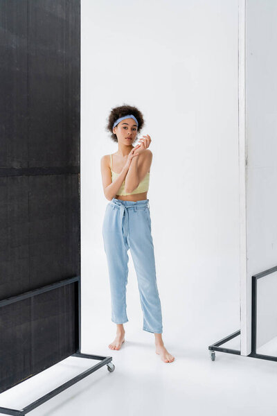Barefoot african american woman in headband and top posing on grey background 