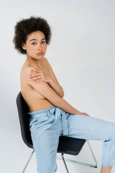 黒っぽいですアフリカ系アメリカ人モデルでパンツで椅子に座っグレーの背景 — ストック写真