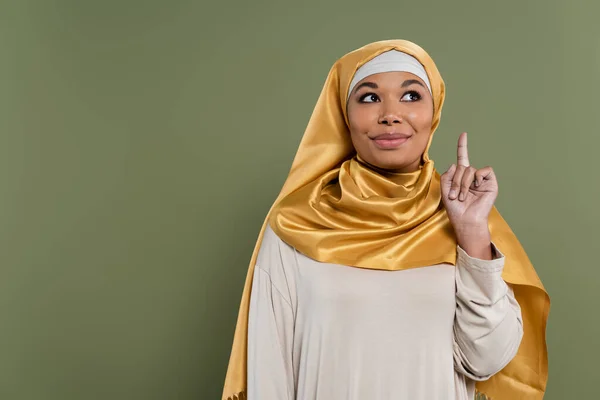 Smiling multiracial woman in hijab having idea isolated on green