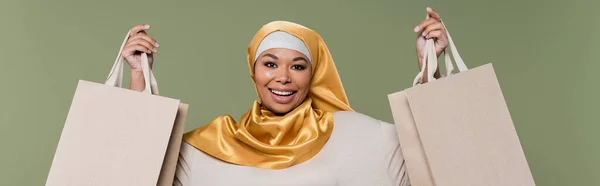 Mujer Multirracial Despreocupada Hijab Sosteniendo Bolsas Compras Aisladas Verde Pancarta —  Fotos de Stock