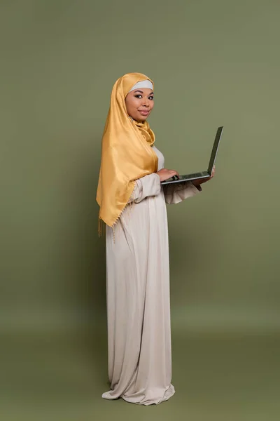 Νεαρή Πολυφυλετική Γυναίκα Μαντίλα Που Χρησιμοποιεί Φορητό Υπολογιστή Πράσινο Φόντο — Φωτογραφία Αρχείου