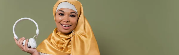 Perempuan Multirasial Yang Riang Mengenakan Jilbab Memegang Headphone Nirkabel Yang — Stok Foto