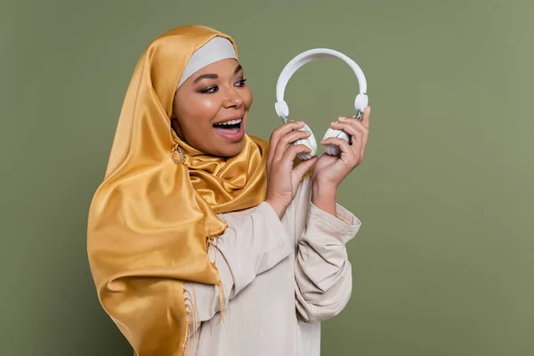 Perempuan Multirasial Ceria Dalam Jilbab Memegang Headphone Terisolasi Hijau — Stok Foto
