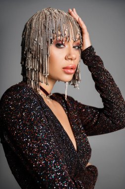 Gri peruklu ve siyah lurex elbiseli seksi genç kadın portresi. Gri renkli kameraya bakıyor.