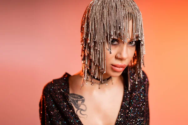 stock image portrait of sexy tattooed woman in metallic headwear with rhinestones looking at camera on coral pink background