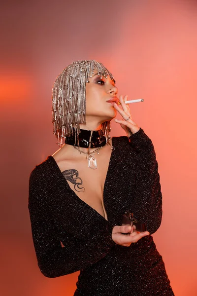 タトゥーのある女性で光沢のあるウィッグと黒セクシードレス喫煙タバコオンピンクとオレンジの背景 — ストック写真